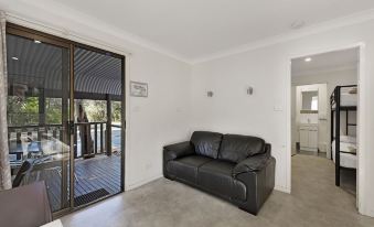 a black couch is sitting in a living room with white walls and a sliding glass door at Discovery Parks - Emerald Beach
