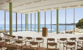 a large conference room with a view of the ocean , where a speaker is standing in the middle of the room at Kempinski Hotel Adriatic Istria Croatia