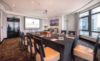 "a conference room with a long table , chairs , and a projector screen displaying the logo "" new york times "" on it" at Cork International Hotel
