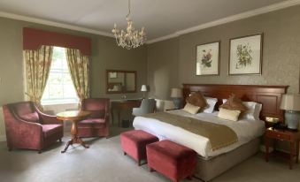 a luxurious hotel room with a king - sized bed , two chairs , and a chandelier , all set against a gray carpet at Leixlip Manor Hotel
