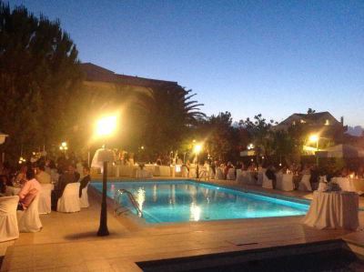 a large outdoor event with a swimming pool , palm trees , and people walking around at dusk at Hotel Summery