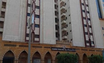 There is a building with an arch in front and a large white sign on the side at Al-Qasswa Towers Hotels