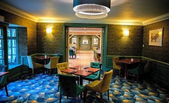 a modern bar with green and blue carpeting , gold chandeliers , wooden tables , chairs , and a chandelier at The Holt Hotel