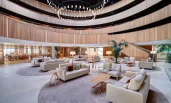 a large , modern hotel lobby with various seating arrangements and a circular ceiling made of wood at Protur Biomar Sensatori Resort