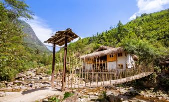 a wooden bridge spanning a river , leading to a traditional thatched - roof house in the mountains at Topas Riverside Lodge