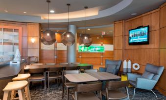 a modern cafe with wooden walls , large screens , and various seating arrangements , including tables and chairs at SpringHill Suites Detroit Auburn Hills