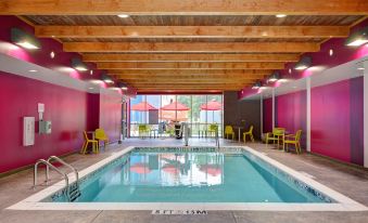a large swimming pool with pink walls and yellow umbrellas , surrounded by chairs and tables at Home2 Suites by Hilton Fort Mill