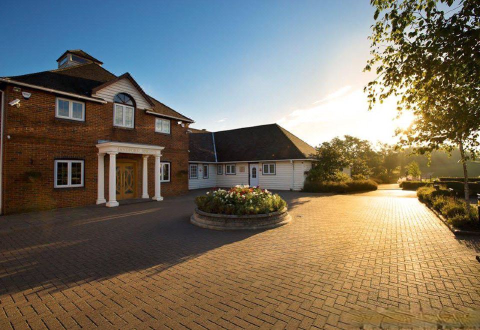 a large brick building with a well - maintained flower garden in front of it , under the setting sun at Sandford Springs Hotel and Golf Club