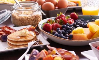 a variety of breakfast foods , including pancakes , eggs , and fruit , arranged on a table for a meal at Hyatt Place Melbourne / Palm Bay / I-95