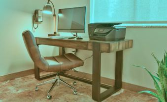 a computer desk with a printer and monitor , along with a chair , in a room with a window at GrandStay Hotel & Suites