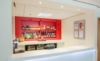 a bar with a red wall and shelves of bottles , next to a white counter at Travelodge Slough