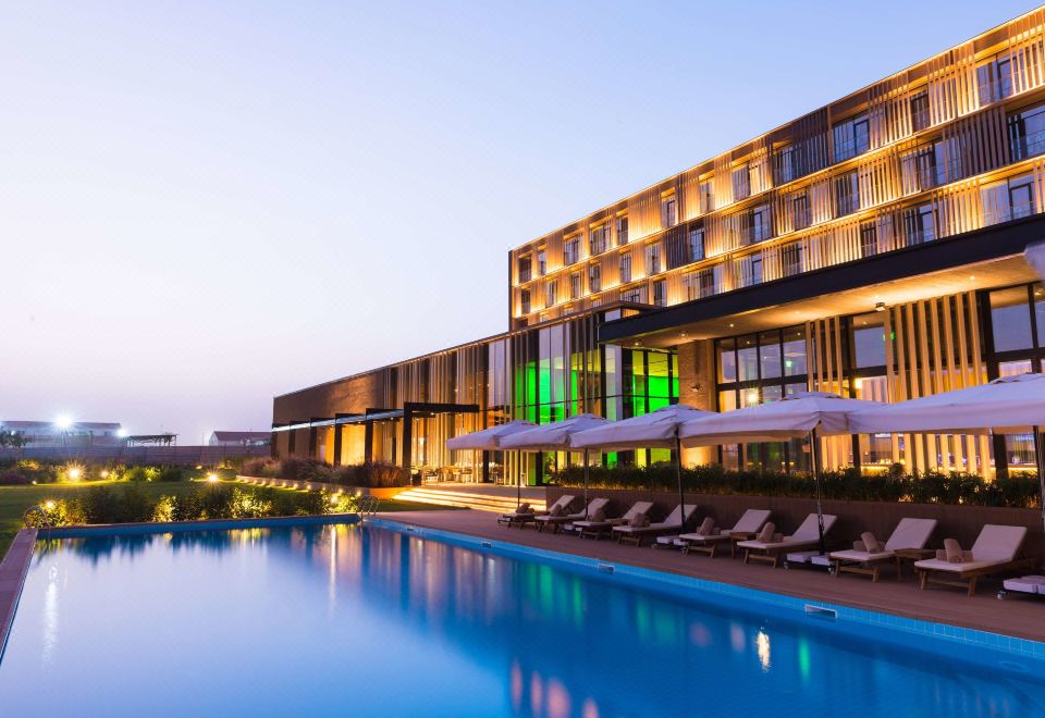 a large hotel with a swimming pool in front of it , surrounded by chairs and umbrellas at Radisson Hotel, Dakar Diamniadio