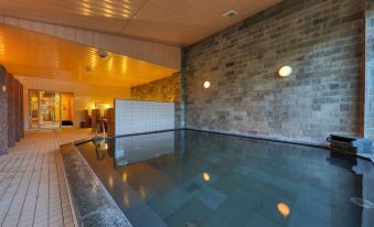 a modern indoor swimming pool with stone walls , wooden ceiling , and lit windows , giving it a cozy and inviting atmosphere at Fuji Matsuzono Hotel