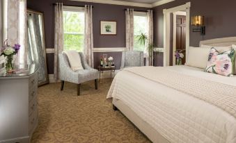 a luxurious bedroom with a large bed , two armchairs , and a window with curtains , all set against a dark purple wall at The Jacqueline House of Wilmington