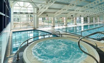 a large indoor swimming pool with a hot tub and lounge chairs , surrounded by glass windows at Crieff Hydro