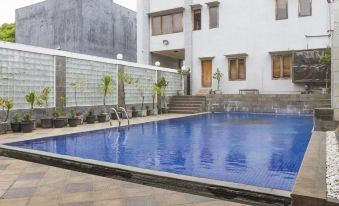 a large blue swimming pool surrounded by a building , with stairs leading up to the entrance at RedDoorz Near Jatinangor Town Square