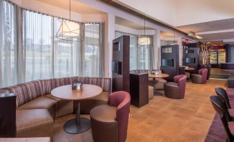a modern lounge area with wooden floors , pink chairs , and couches , as well as a dining table and bar area at Courtyard by Marriott Fairfax Fair Oaks