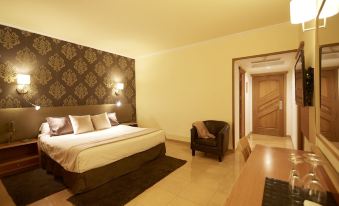 a large bed with white linens is in a room with a chair and a wooden door at Invisa Hotel la Cala