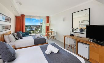 a hotel room with two beds , a desk , and a large window overlooking the ocean at Pelican Waters Resort
