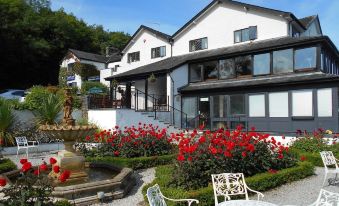 a white house surrounded by a beautiful garden , with red flowers blooming in the yard at Damson Dene Hotel