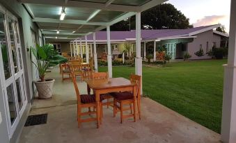 an outdoor dining area with wooden tables and chairs , surrounded by a grassy field and a building at Graceland Guesthouse
