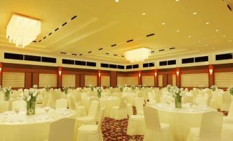 a large banquet hall with white tablecloths and chairs , a chandelier , and paintings on the walls at Grand Asrilia Hotel