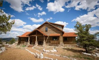 a large wooden house surrounded by a grassy field , with a cloudy sky in the background at Zion Mountain Ranch