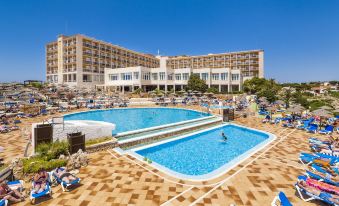 a large hotel with a swimming pool and sun loungers , surrounded by trees and people enjoying the sunny day at Globales Almirante Farragut