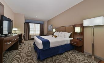 a large bed with a blue blanket and white pillows is in the middle of a room at Best Western Plus Williston Hotel  Suites