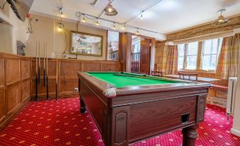 a large pool table surrounded by chairs in a room , with a dining table and chairs nearby at The Crown Hotel