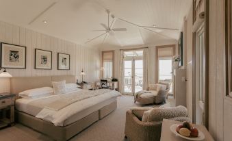 a spacious bedroom with a large bed , two chairs , and a window overlooking the ocean at Rosewood Kauri Cliffs