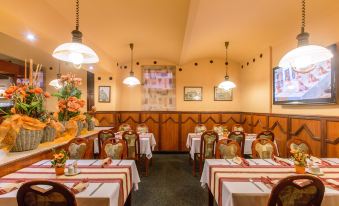 a restaurant with wooden tables and chairs , red and white tablecloths , and a flower arrangement on each table at Hotel Victoria