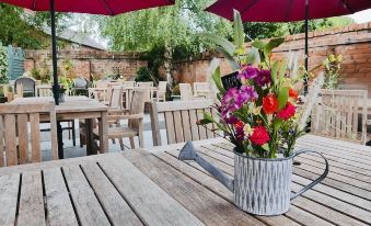 an outdoor dining area with a table , chairs , and umbrellas , surrounded by greenery and a brick building at The Boot Inn