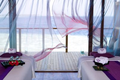 a room with two beds , each covered in white sheets and a purple headboard , is shown with a view of the ocean outside at Vilamendhoo Island Resort & Spa