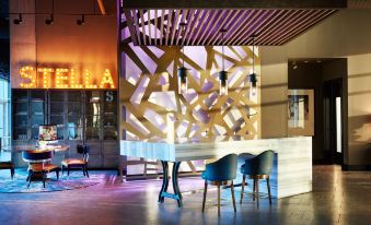 "a modern hotel lobby with a bar area and a neon sign reading "" hotel "" above it" at The Stella Hotel, Autograph Collection