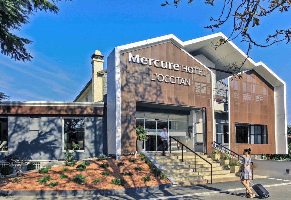 "a modern hotel building with the name "" mercure - hotel bocean "" on it , surrounded by trees and people walking in front of the" at Mercure Castres l'Occitan