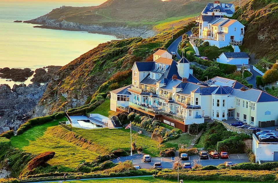 a picturesque coastal town with white buildings , blue roofs , and green mountains , situated on a hill overlooking the ocean at Watersmeet Hotel