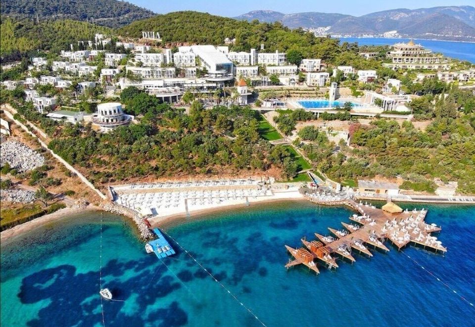 a picturesque beach resort with a large body of water surrounded by buildings , trees , and boats at Duja Bodrum