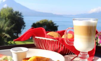 a table with a plate of food , a glass of milk , and a basket of bread near a scenic view at Hotel la Riviera de Atitlán