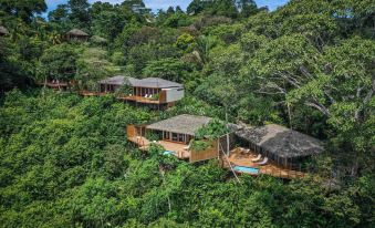 a picturesque mountainous landscape with wooden houses nestled on the side of a mountain , surrounded by lush greenery at Lapa Rios Lodge by Boena