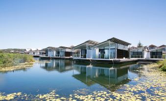 a row of modern houseboats floating on a body of water , surrounded by greenery and blue sky at Caves Coastal Bar & Bungalows