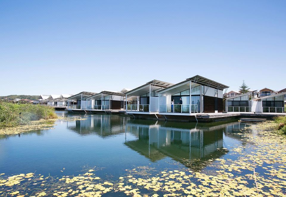 a row of modern houses on stilts over a body of water , with greenery in the background at Caves Coastal Bar & Bungalows