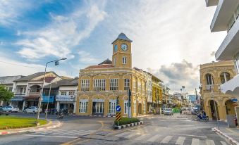 A large building with a clock tower stands on the corner, while cars drive down an empty street at B2 Phuket Premier Hotel
