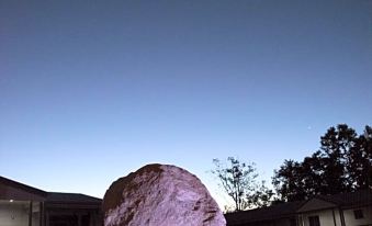 a large rock is sitting in the foreground with a house and trees in the background at The Rocks Motel