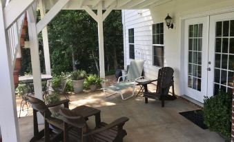 a white house with a porch , featuring several chairs and potted plants , providing a comfortable outdoor living space at A Mighty Oak B&B