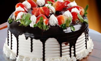 a large chocolate cake with strawberries and whipped cream on top , sitting on a dining table at Hotel Rivoli