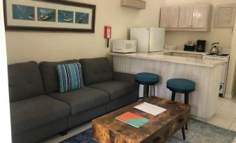 a living room with a gray couch , wooden coffee table , and blue stools near a kitchenette at Regent Apartments