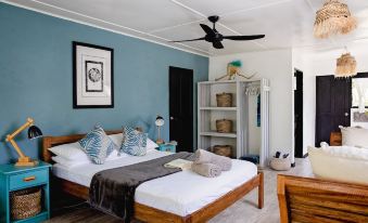 a bedroom with a wooden bed , blue walls , and a black wall hanging , along with a fan on the ceiling at Turtle Bay Lodge