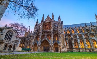 a beautiful gothic cathedral surrounded by trees and grass , with the sun setting in the background at President Hotel