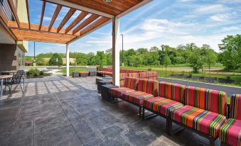 a covered patio with multiple benches , surrounded by trees and a body of water , under a wooden roof at Home2 Suites by Hilton Mechanicsburg
